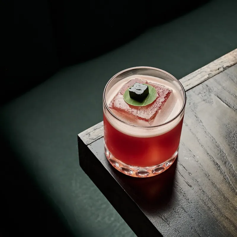A red cocktail with a large ice cube